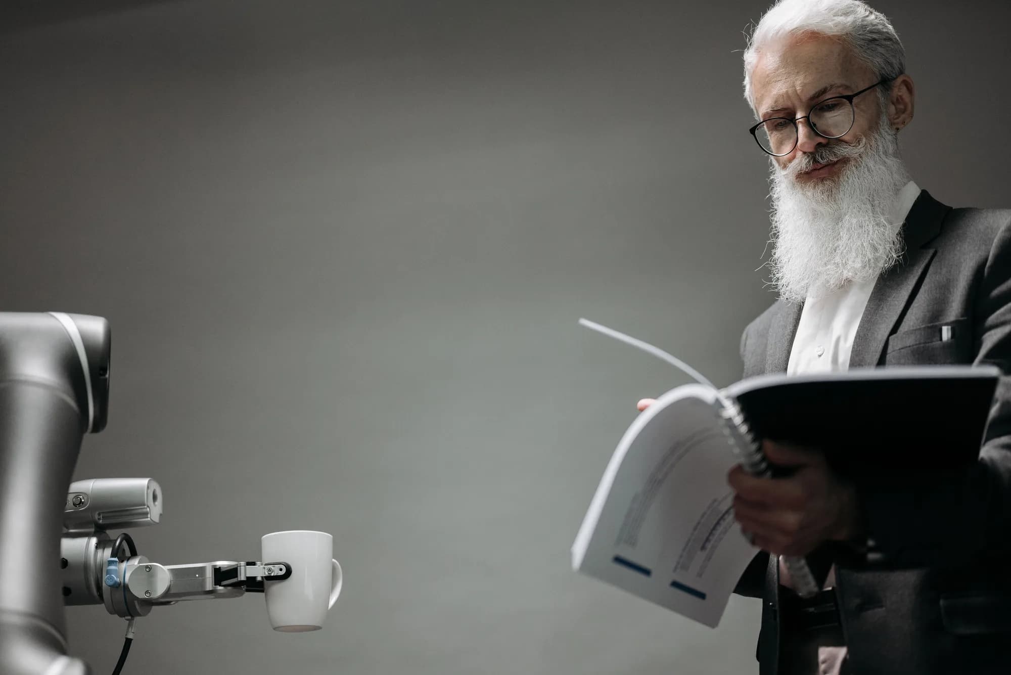 A man reading a document beside a robotic arm on a workbench